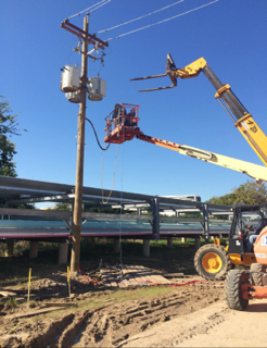 A crew in a lift on overhead distribution at a pole with a transformer bank and primary connections.