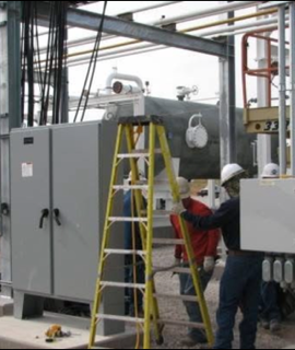 Electricians on a panel and junction boxes inside an industrial structure — the trade work, at the equipment.